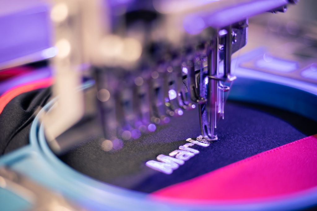 Machine à broder brodant un prénom sur un textile bleu marine à l'atelier K'do Perso